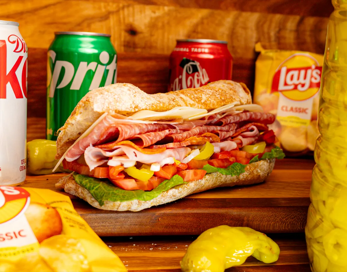 A deli sandwich with chips and drinks photographed for Luigi's Gourmet
